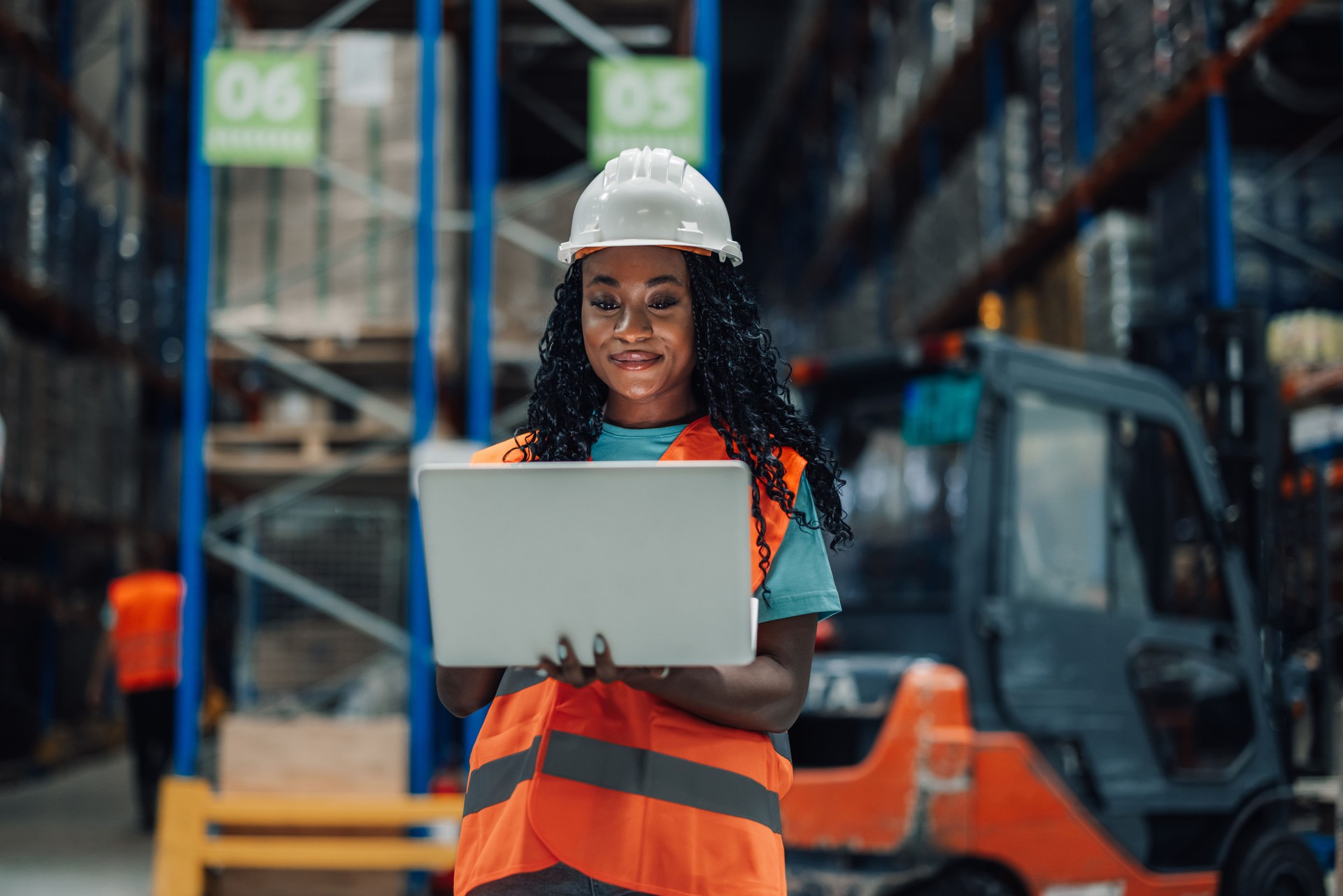 Warehouse worker smiling and using laptop in busy warehouse